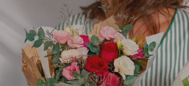Florista de camisa listrada segurando um buquê de lisiantos cor-de-rosa, rosas vermelhas e rosas brancas com eucalipto